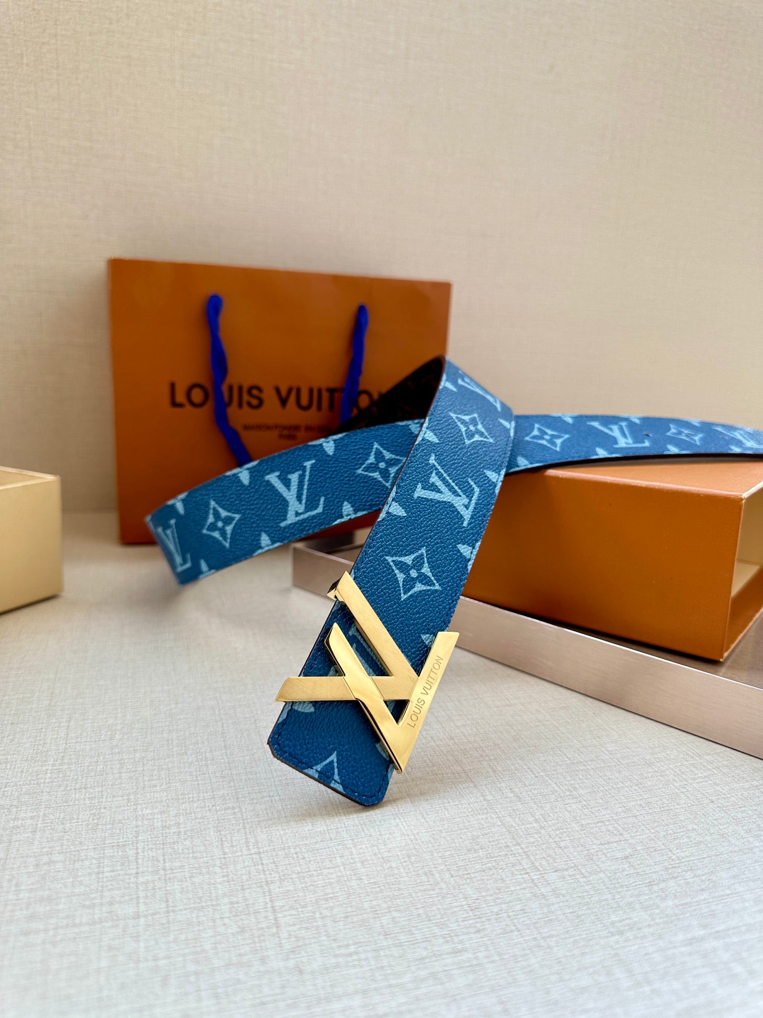 Blue monogram belt with gold-toned LV buckle resting on display boxes