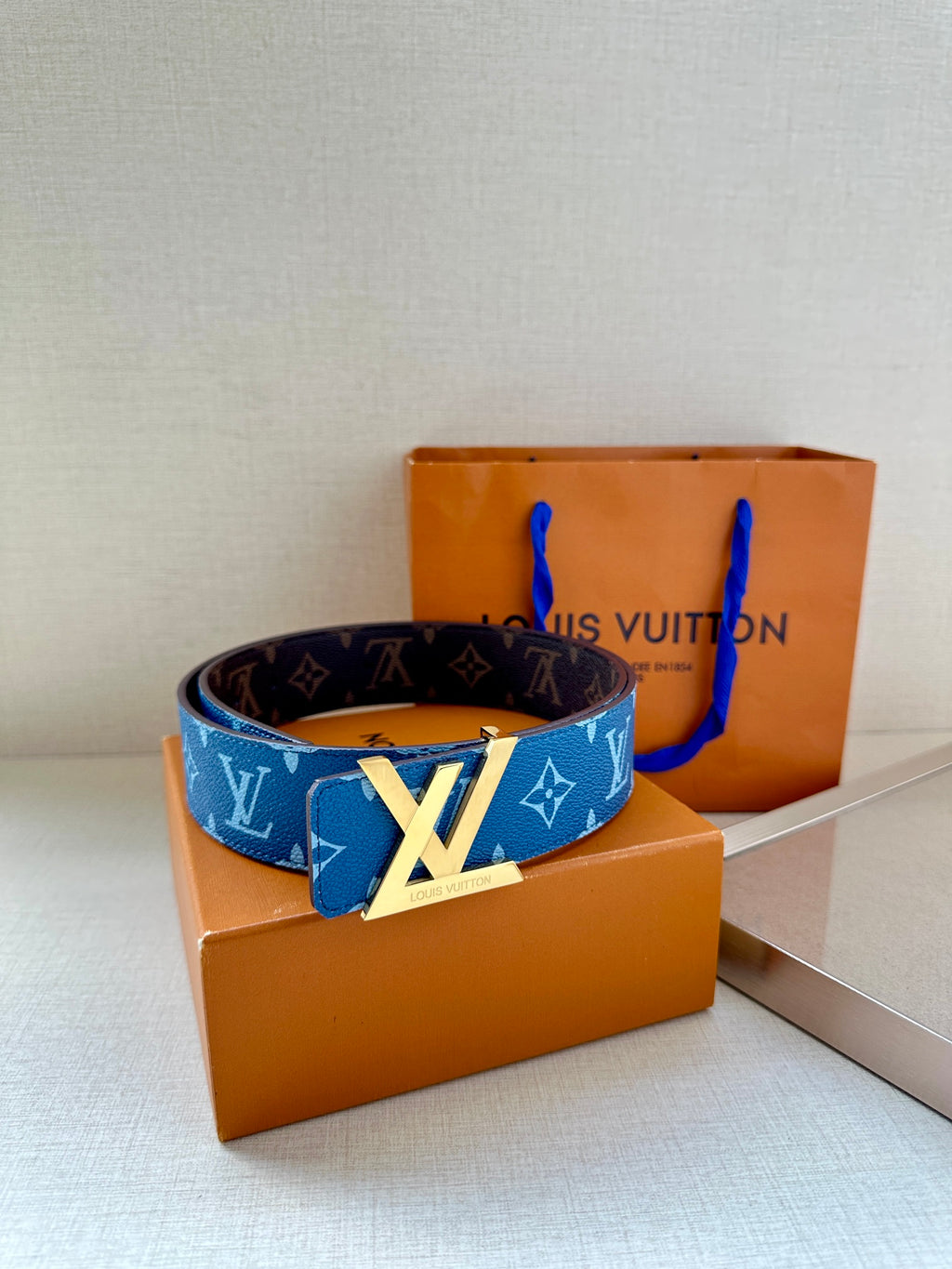 Blue monogram belt with gold-toned LV buckle laid over a box