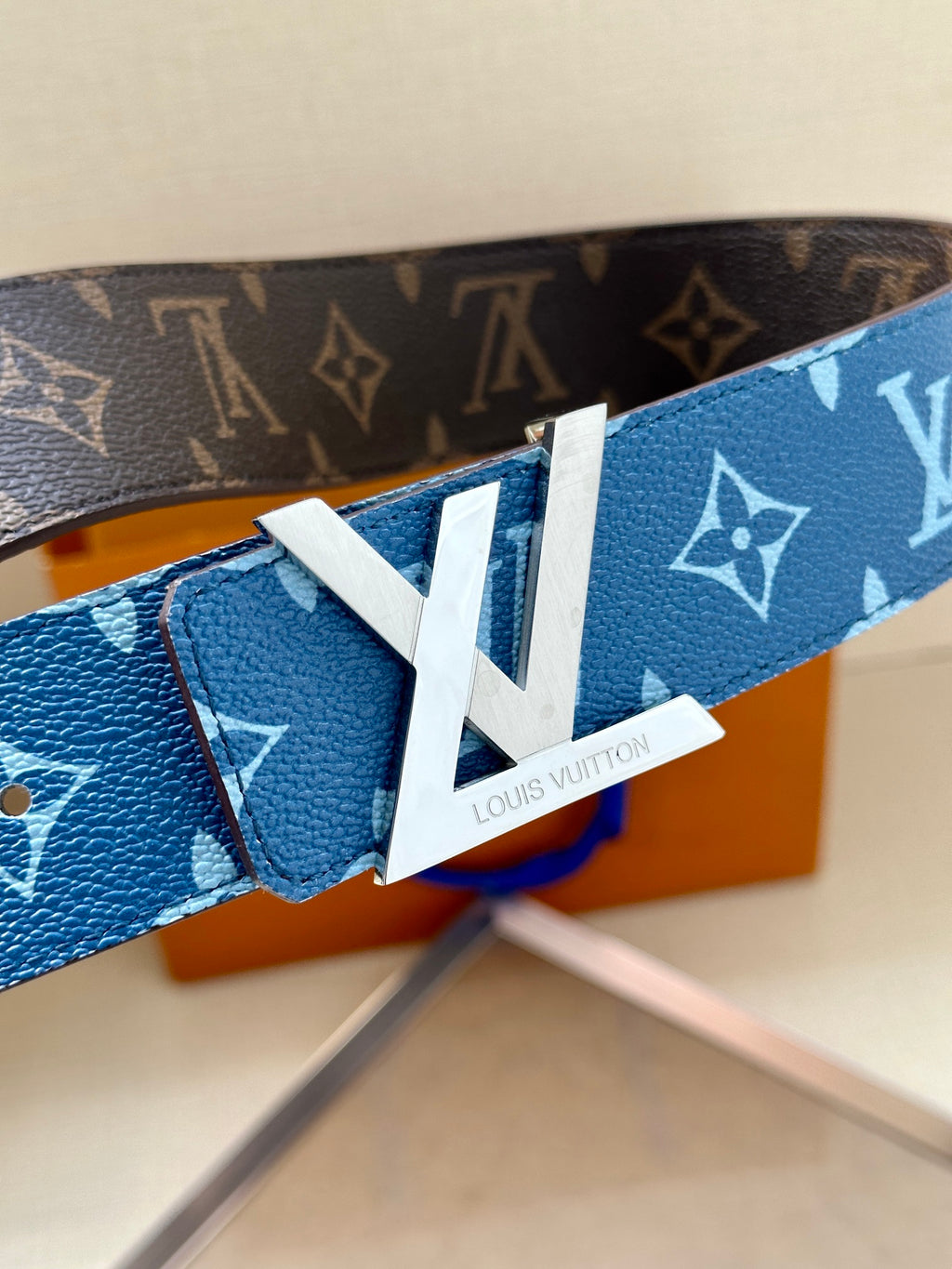 Blue monogram belt close-up with white LV tab and gold-toned buckle
