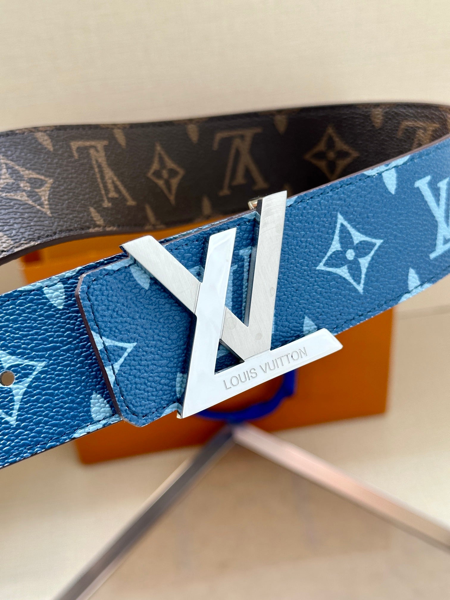 Blue monogram belt close-up with white LV tab and gold-toned buckle