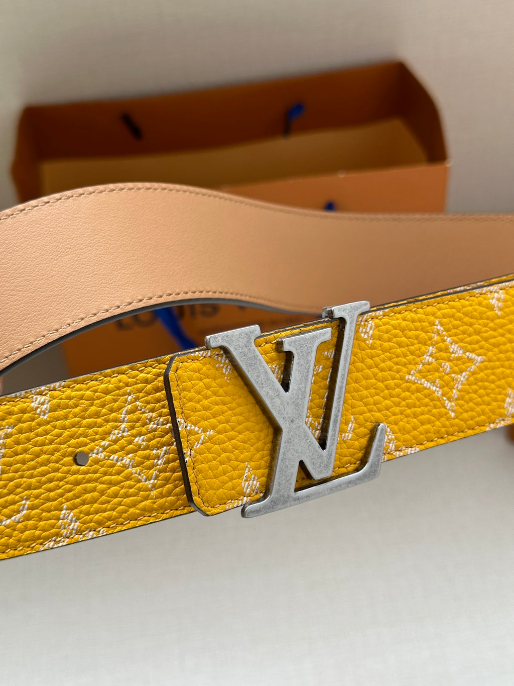 Yellow patterned leather belt with silver LV buckle close-up