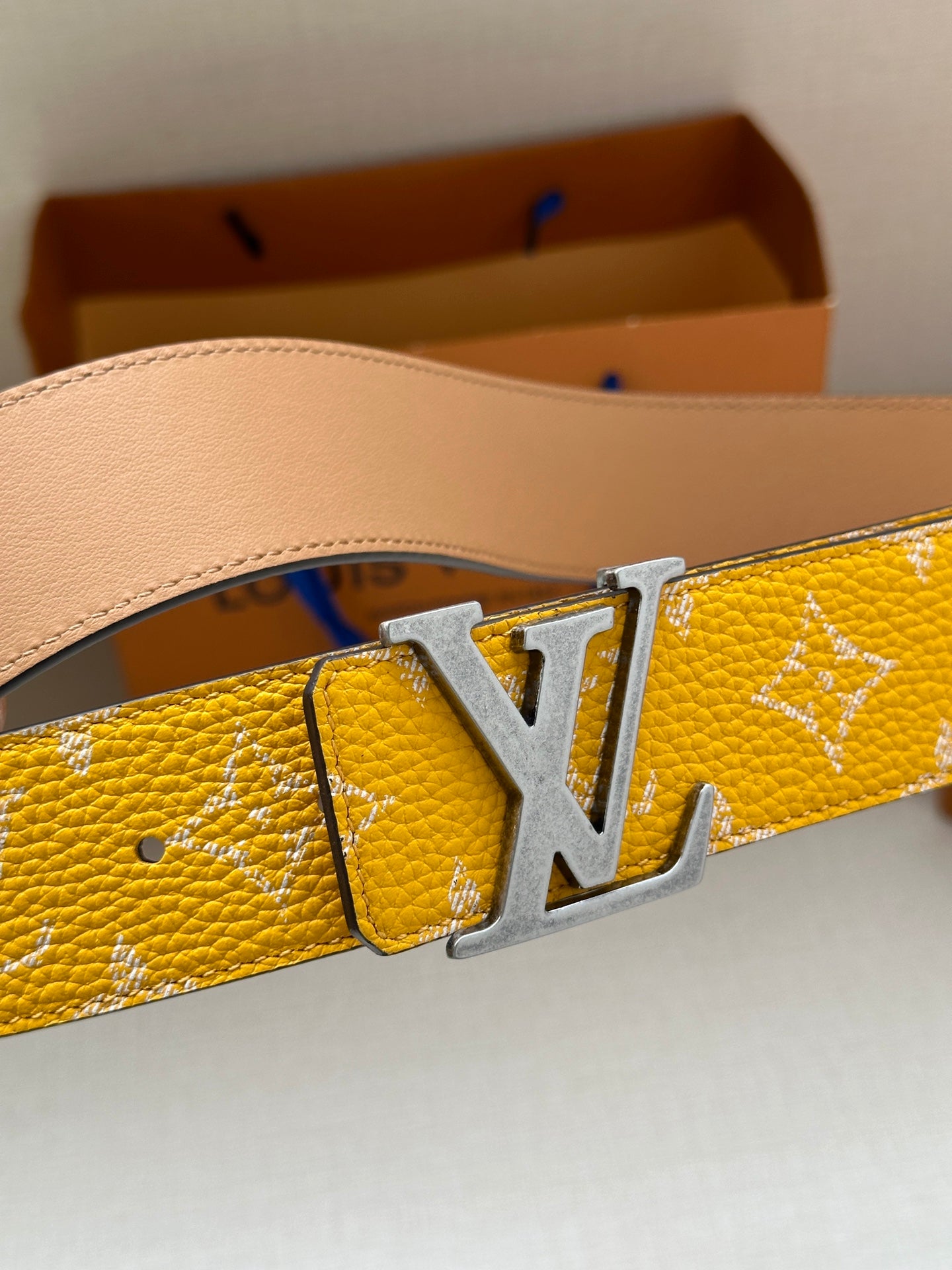 Yellow patterned leather belt with silver LV buckle close-up