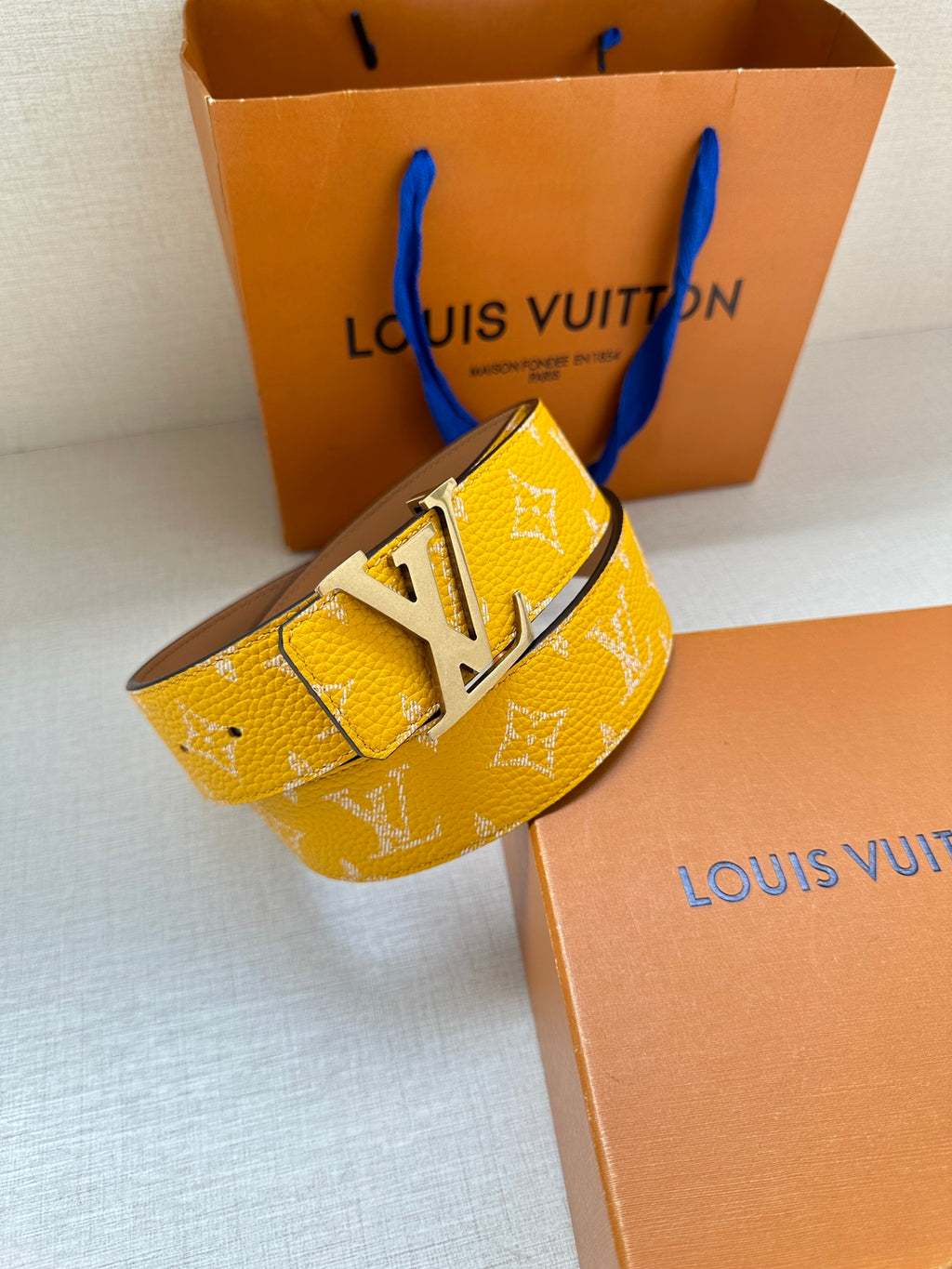 Yellow monogram leather belt with silver LV buckle, angled view