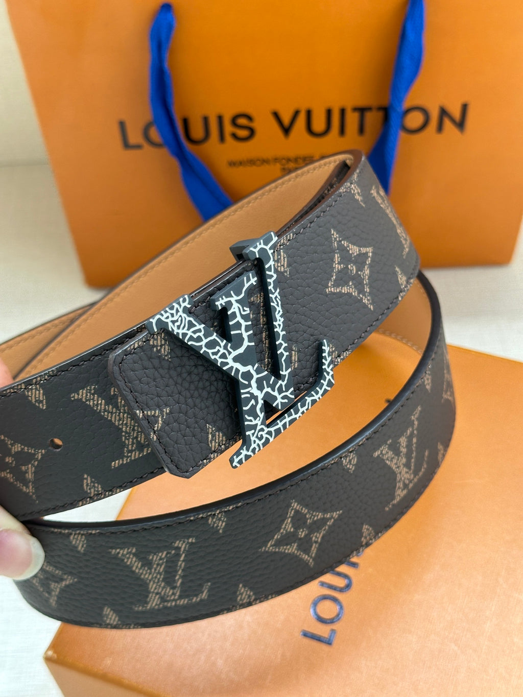 Louis Vuitton monogram belt close-up with dark patterned strap, tan underside, and gold buckle