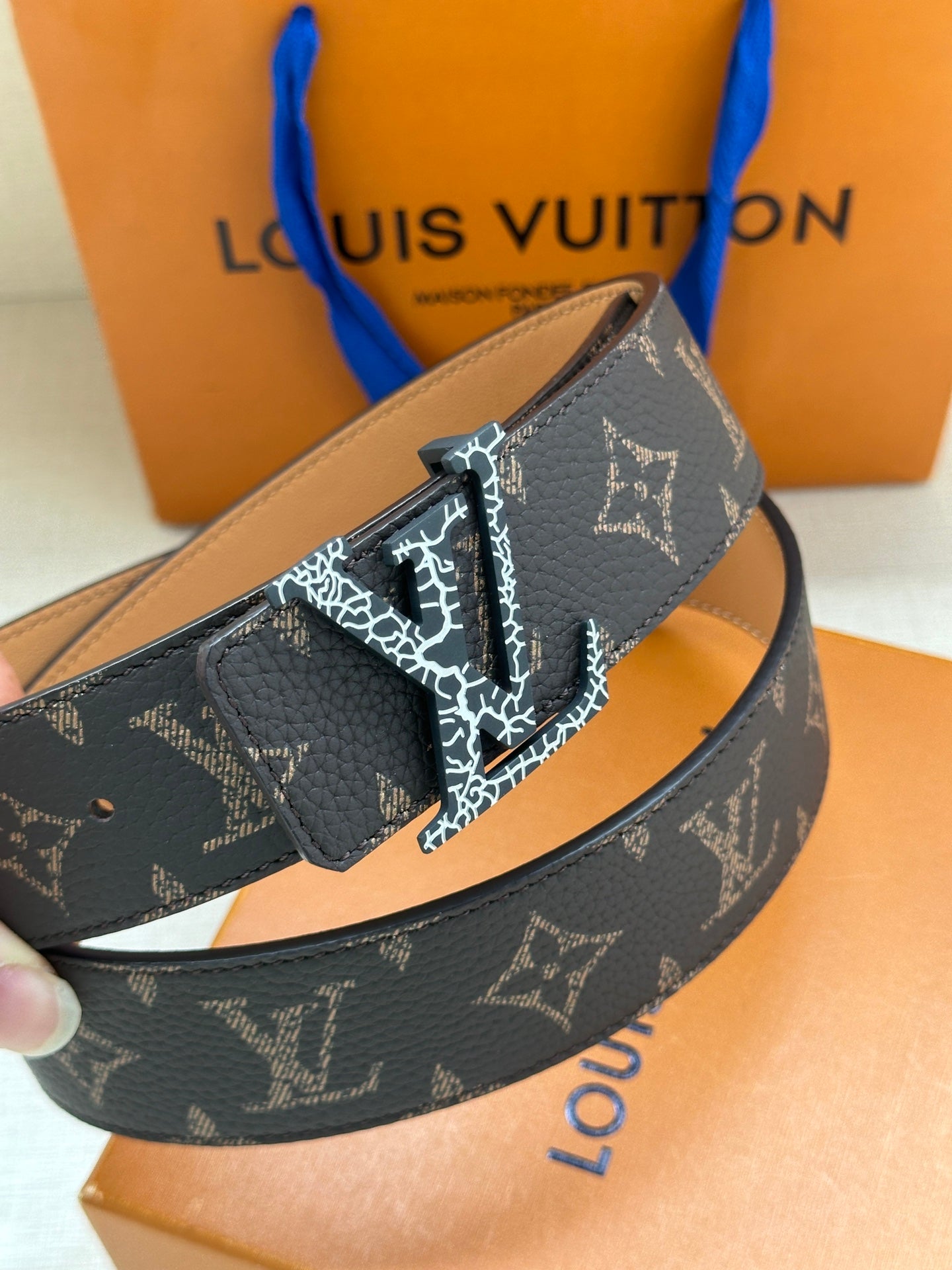 Louis Vuitton monogram belt close-up with dark patterned strap, tan underside, and gold buckle
