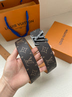 Louis Vuitton monogram belt held in hand with dark patterned strap and gold-tone buckle