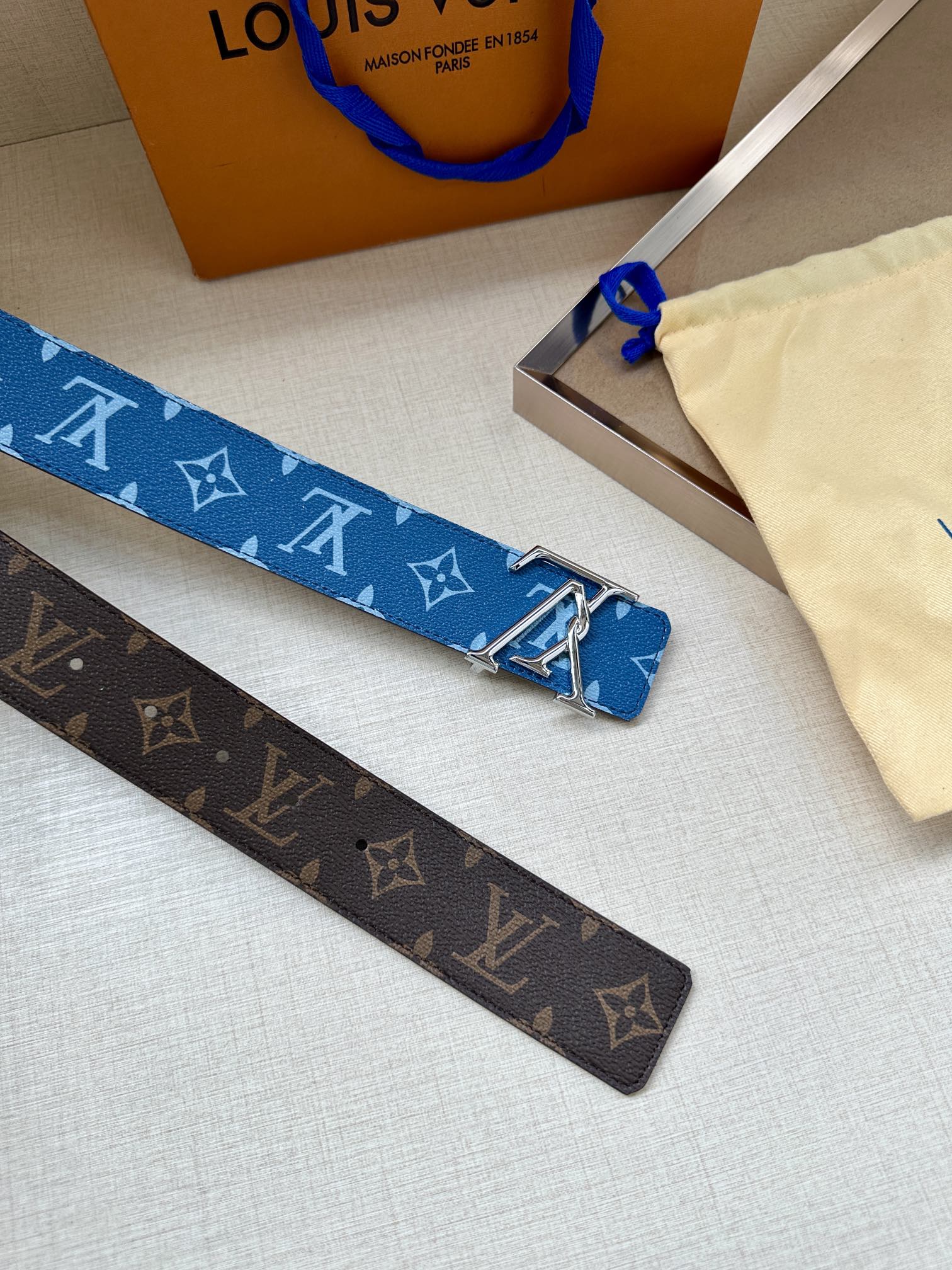 Louis Vuitton monogram belts in blue and brown with silver LV buckles, patterned.