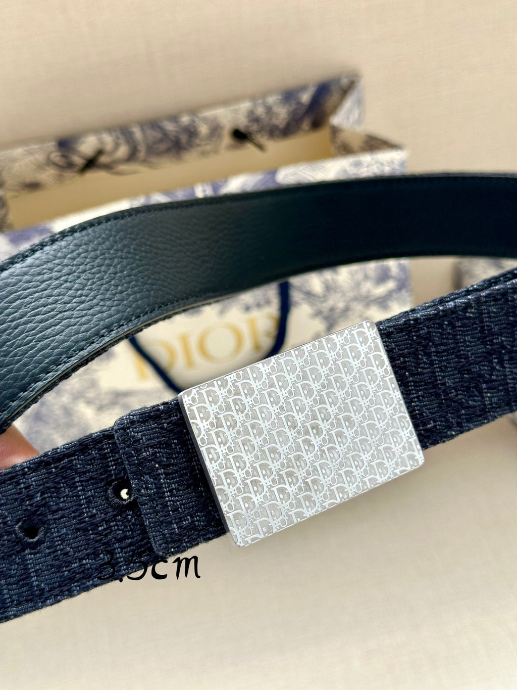 Navy leather belt with silver rectangular patterned buckle, close-up detail.