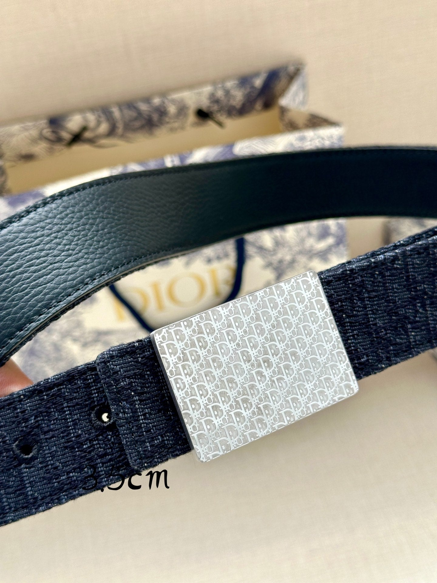 Navy leather belt with silver rectangular patterned buckle, close-up detail.