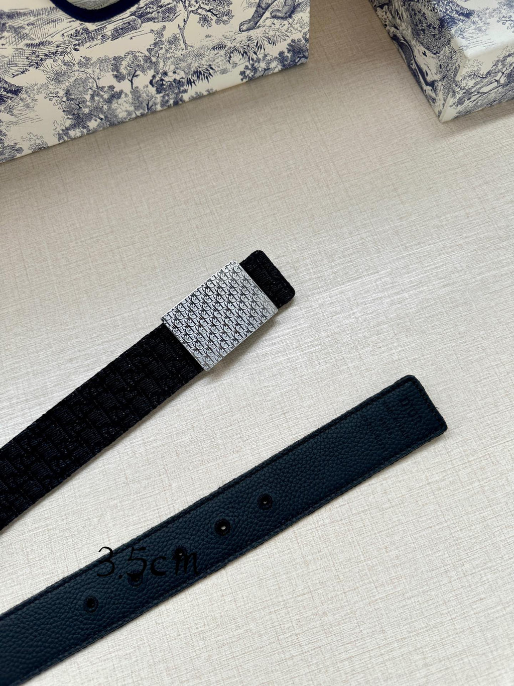 Navy leather belt with silver buckle section and strap with adjustment holes, side view.