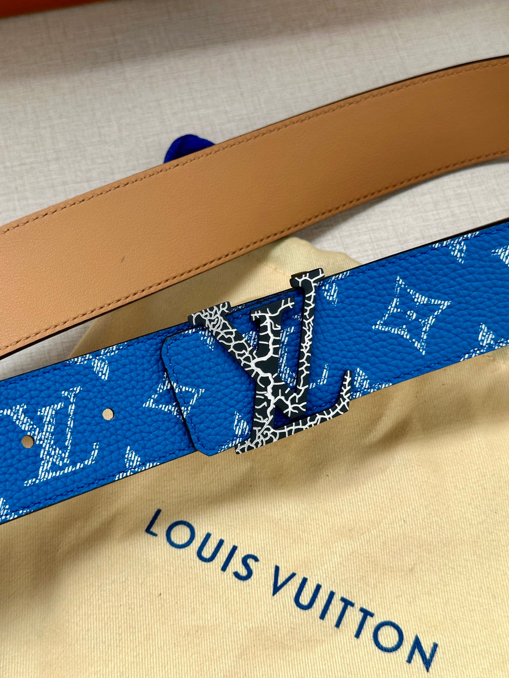 Blue monogram belt close-up with metal buckle and tan leather strap
