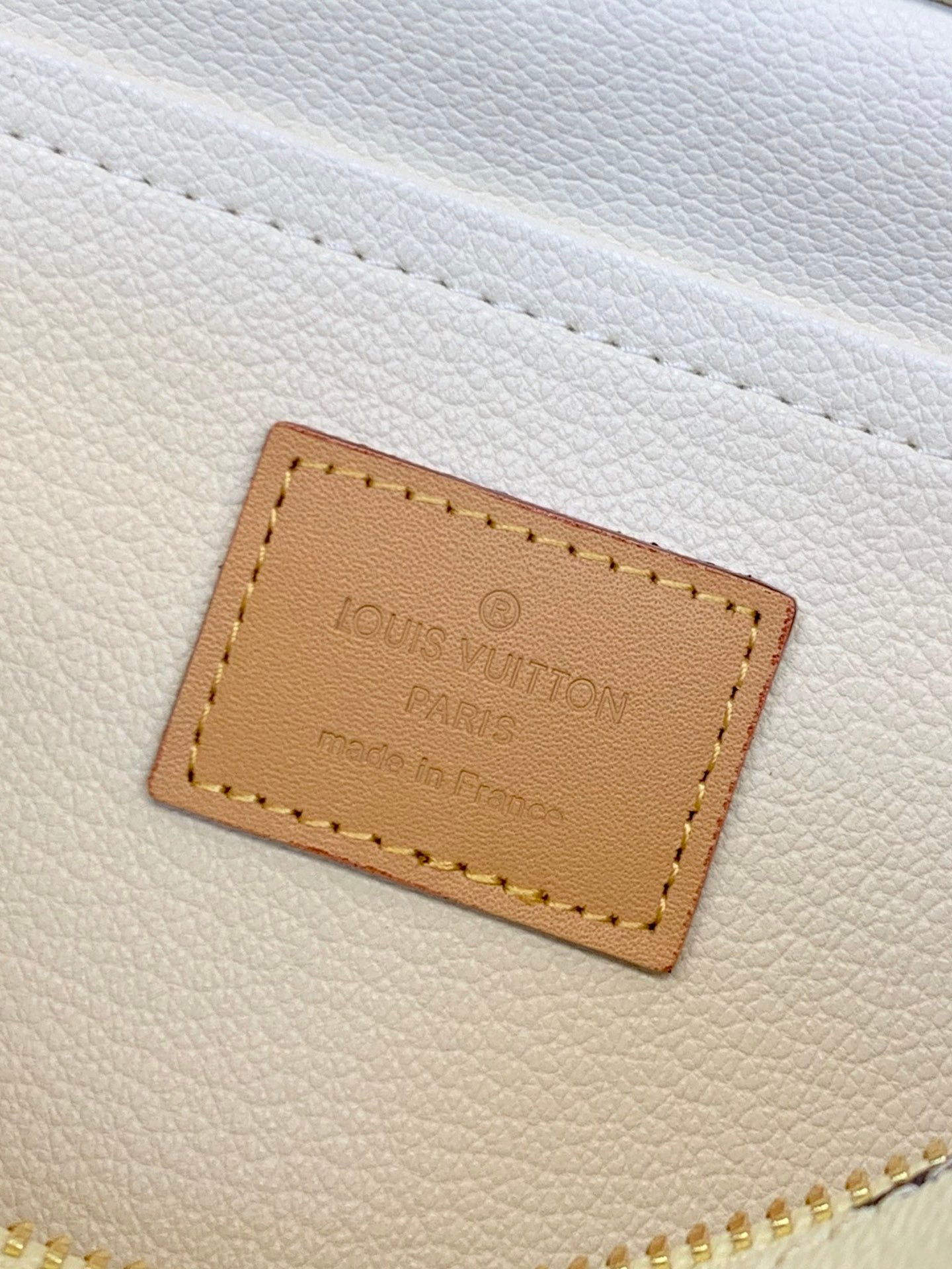 Louis Vuitton logo leather label on white bag surface, tan stitched border