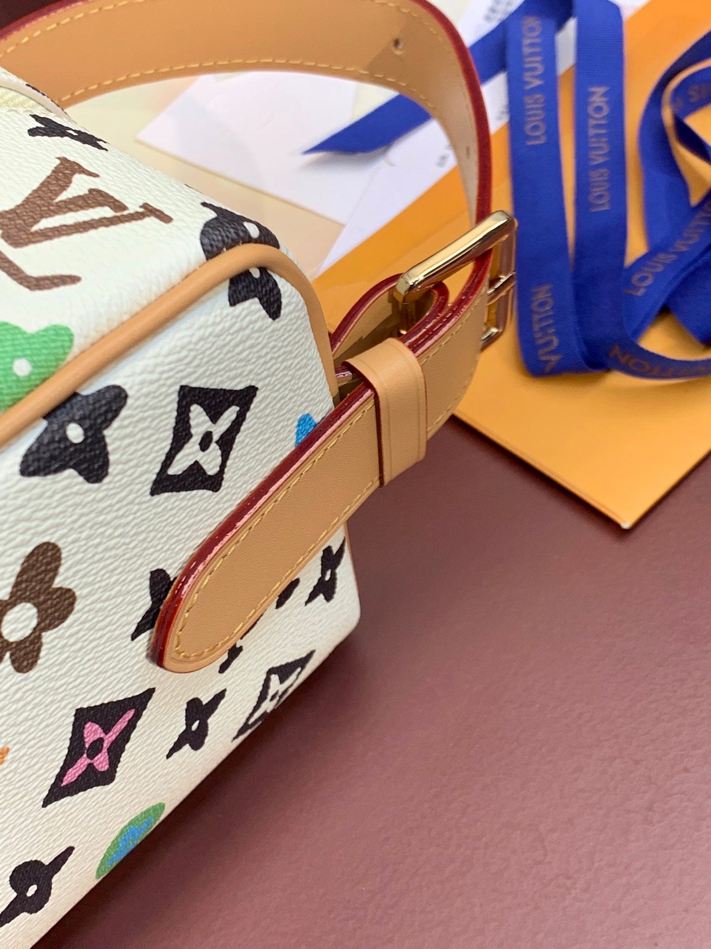 Louis Vuitton strap close-up with tan leather and gold buckle on multicolor monogram canvas