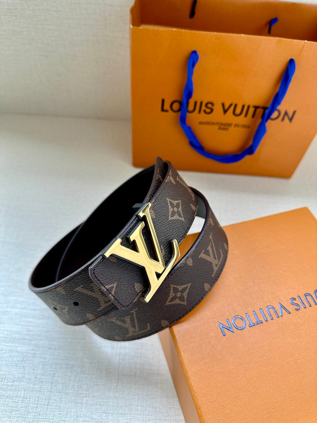 Louis Vuitton monogram belt with LV buckle, angled view on dark strap