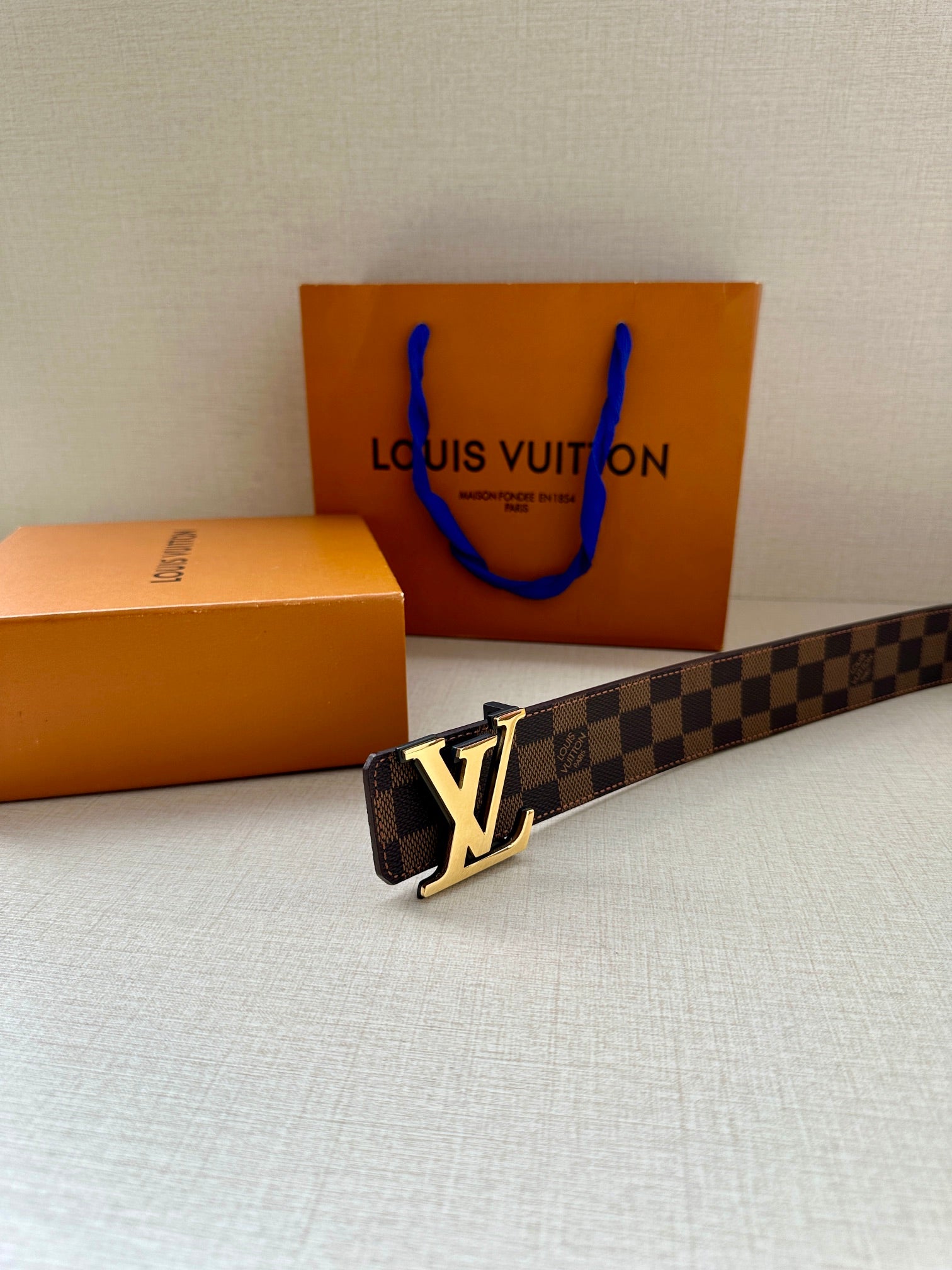 Louis Vuitton belt with damier pattern and gold-tone LV buckle, lying diagonally