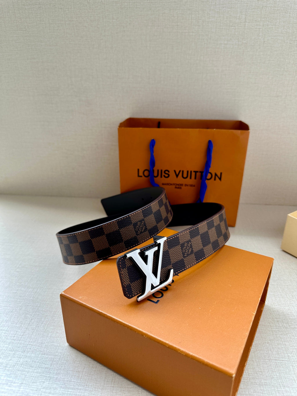 Louis Vuitton damier belt with gold-tone LV buckle and dark interior, laid on box