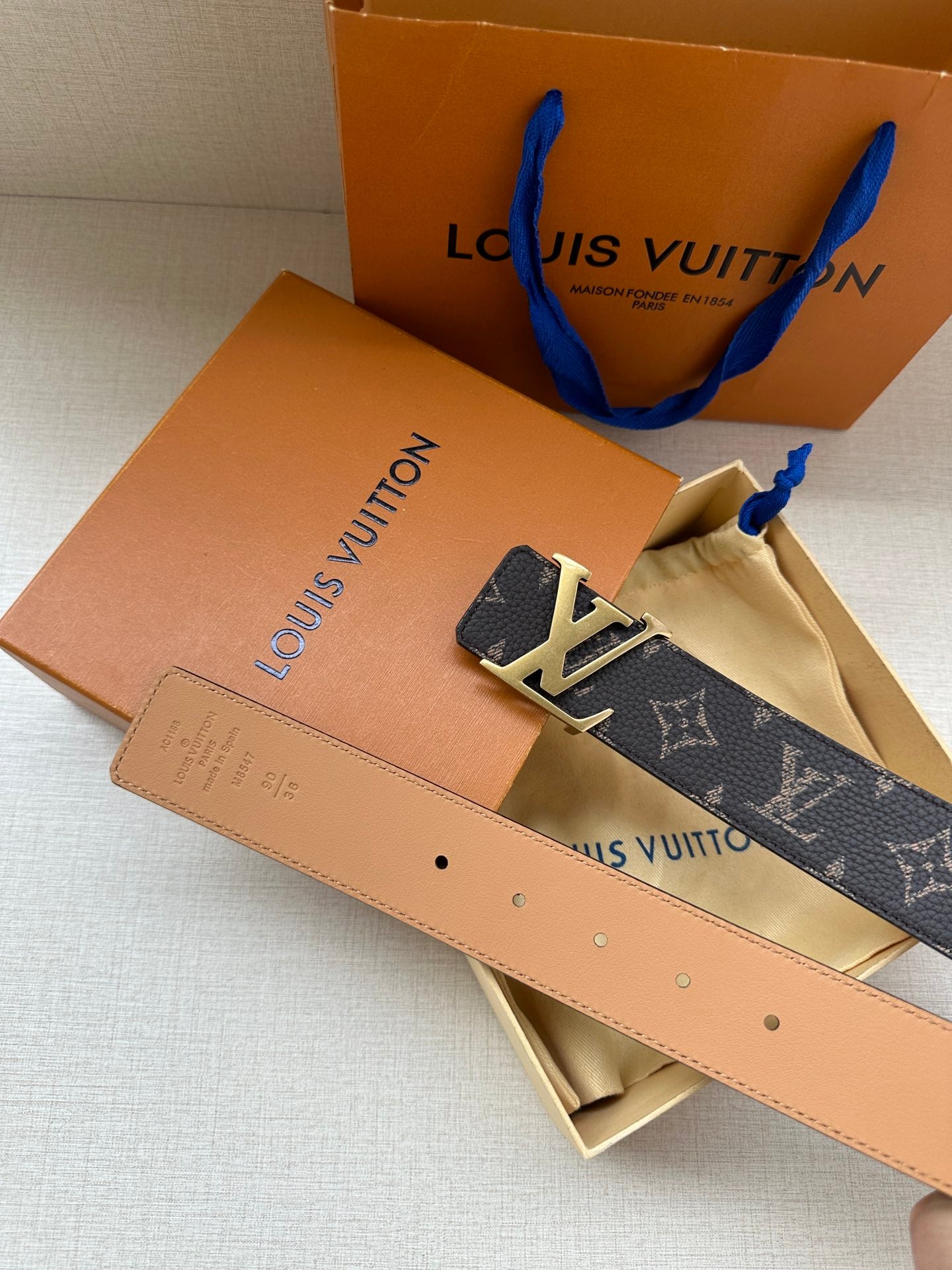 Louis Vuitton belt laid flat, monogram canvas front with silver LV buckle and tan leather reverse.