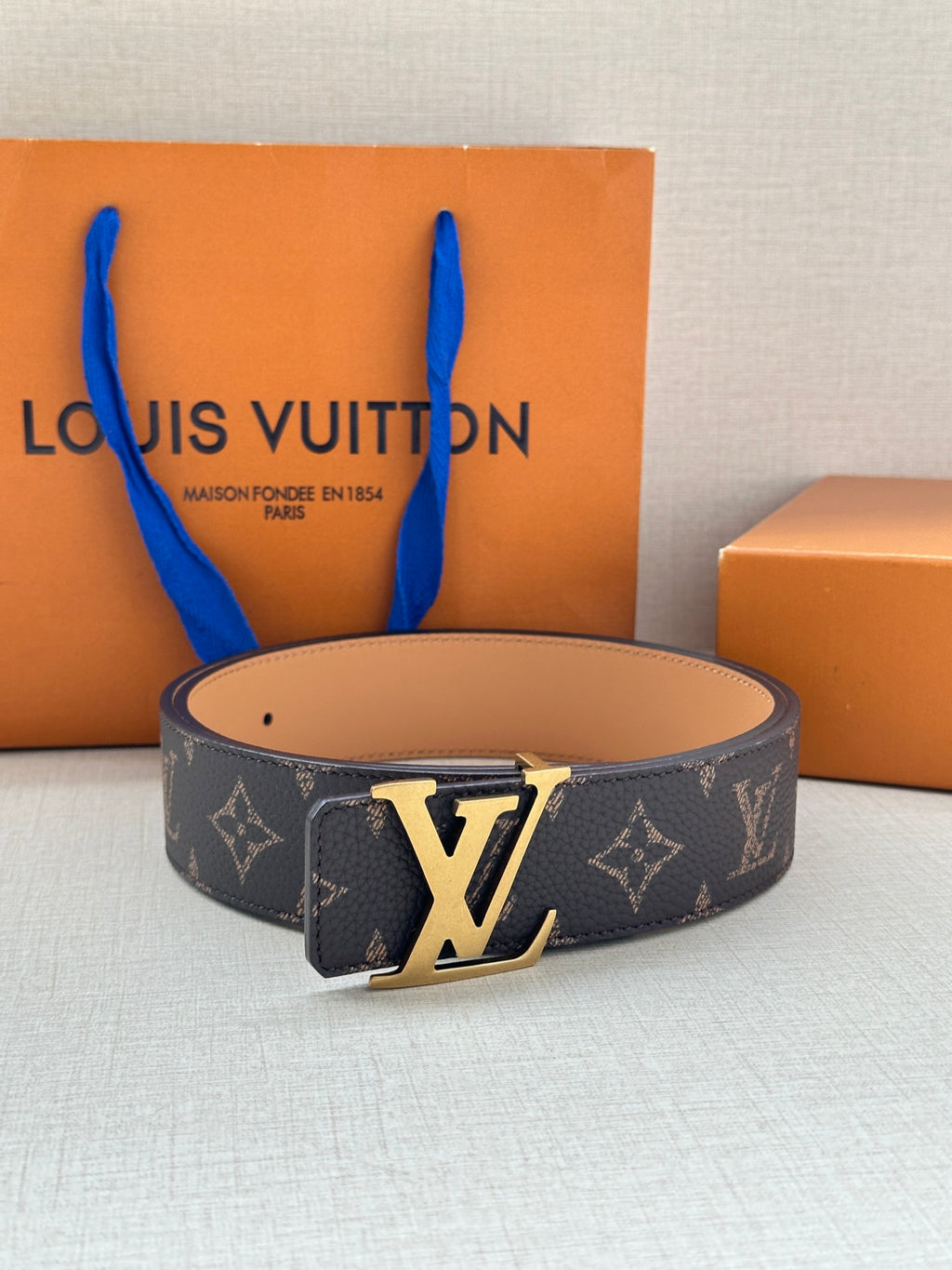 Louis Vuitton monogram belt, dark patterned strap with silver LV buckle and smooth tan underside.