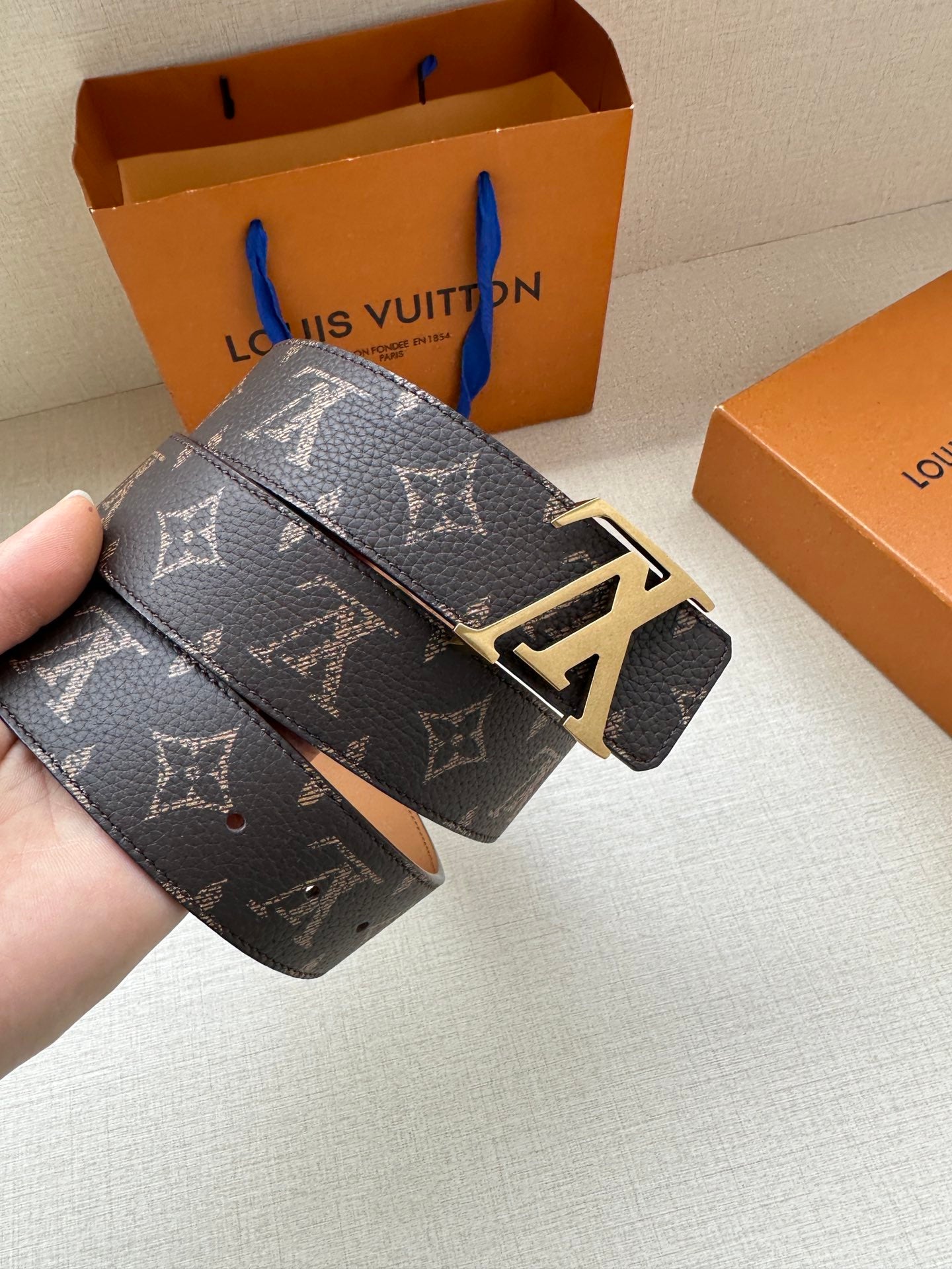 Louis Vuitton monogram belt held in hand, dark canvas strap with silver LV buckle and tan side.