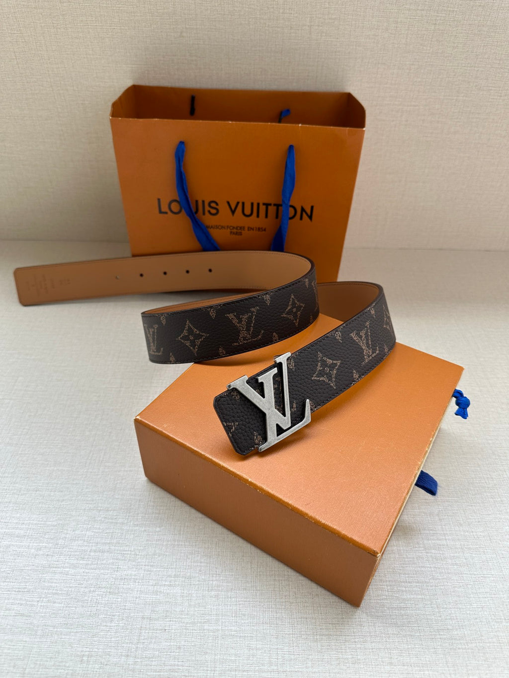 Louis Vuitton monogram belt with silver-tone LV buckle, dark patterned strap and tan inner side.