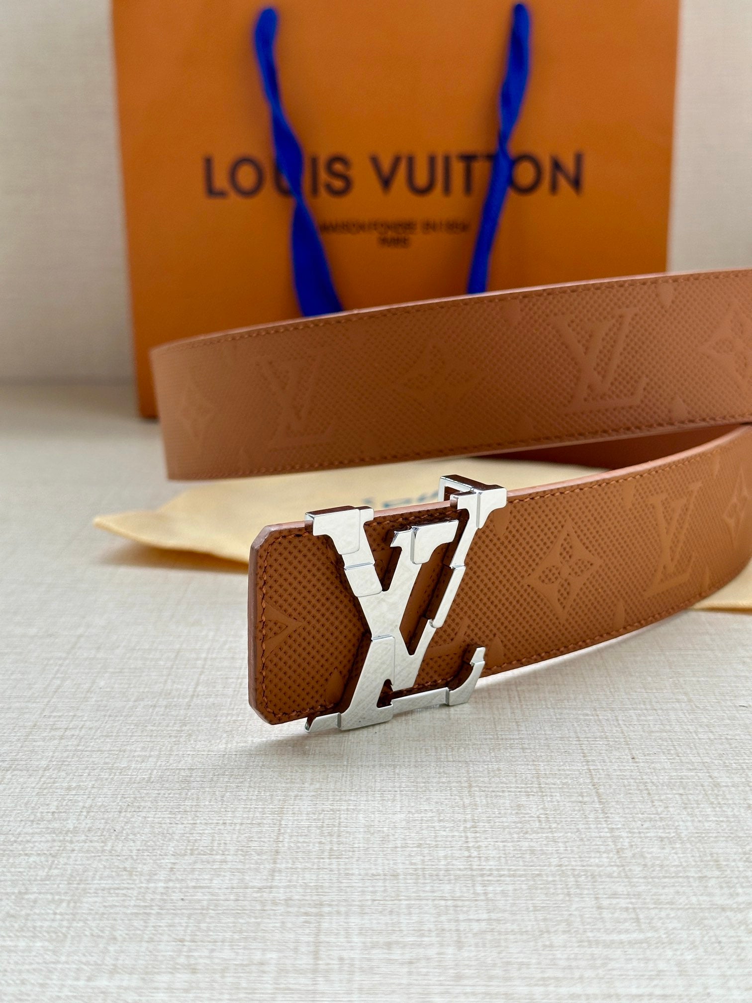 Tan leather belt close-up with silver LV buckle and embossed monogram texture