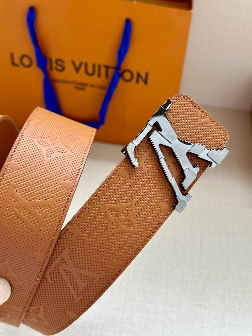 Tan monogram leather belt with silver buckle, shown at an angled close view