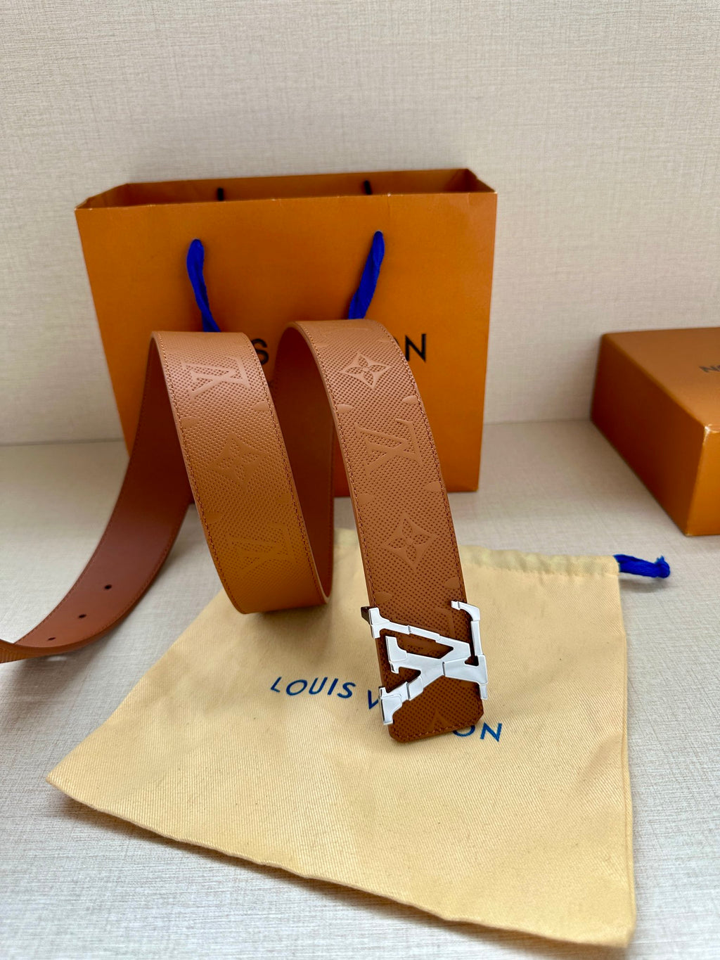 Tan monogram leather belt with silver buckle, dust bag, and Louis Vuitton box