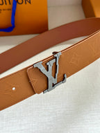 Tan leather belt close-up with silver buckle and embossed monogram pattern