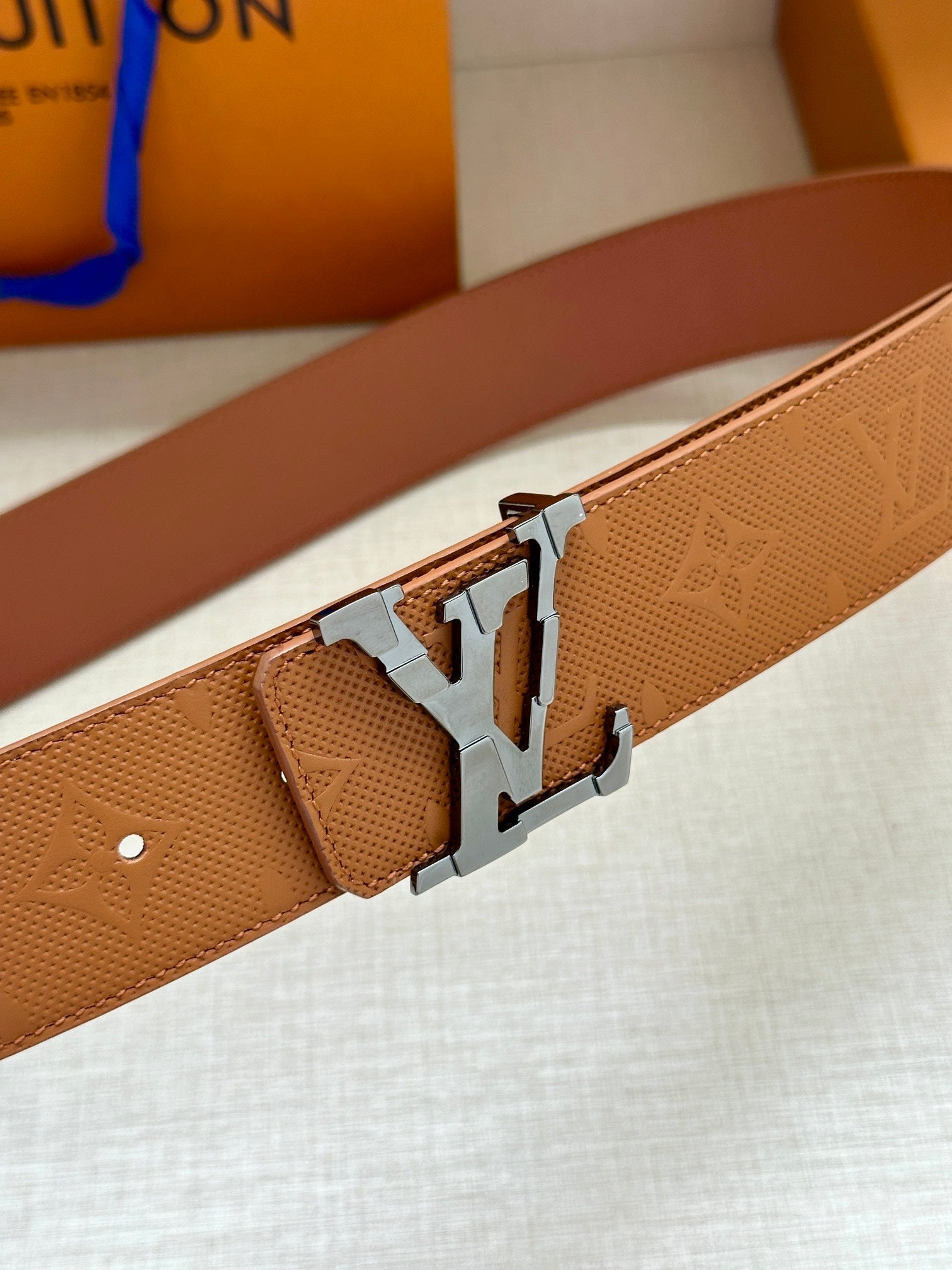 Tan leather belt close-up with silver buckle and embossed monogram pattern