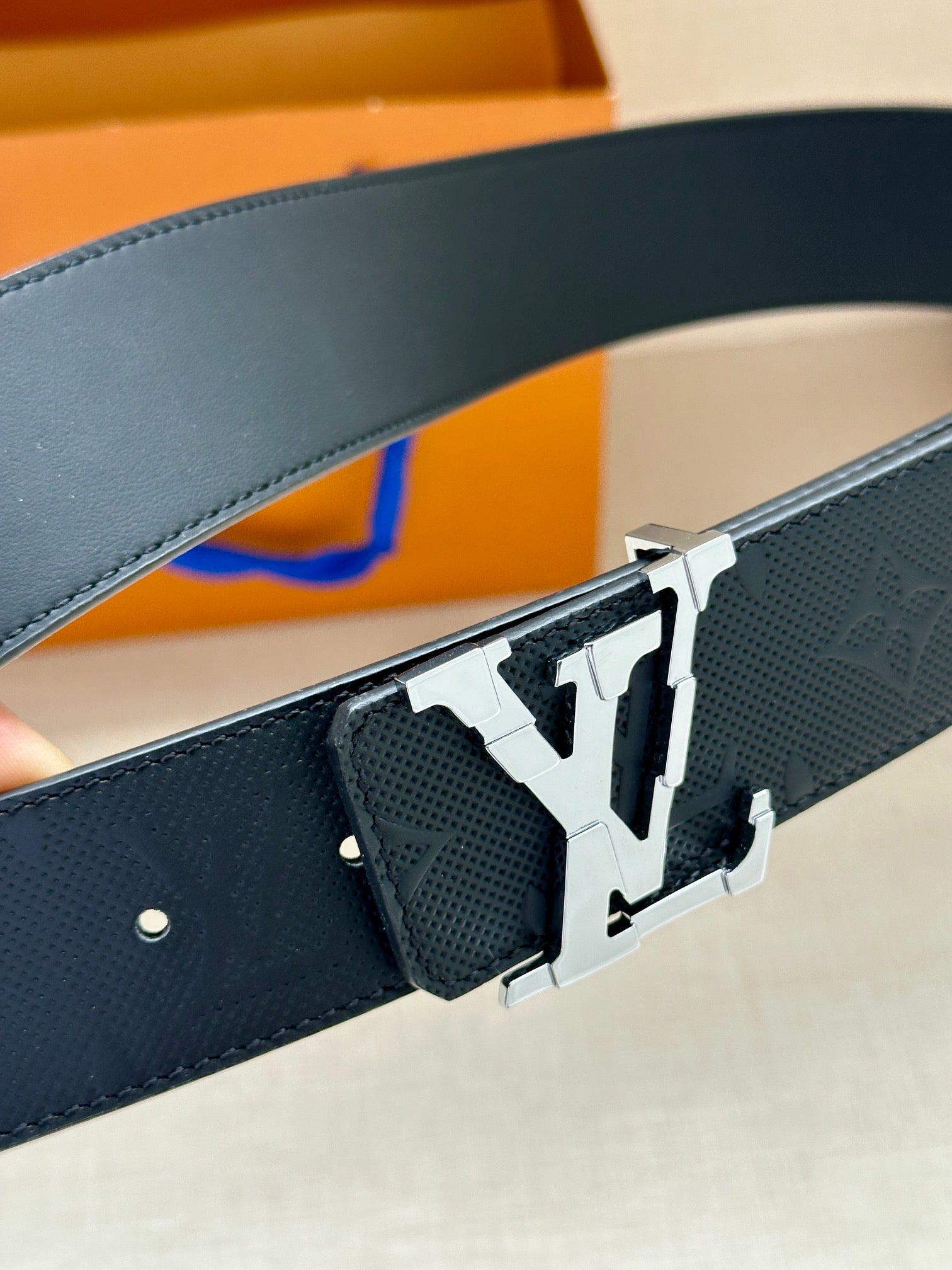 Dark blue leather belt with embossed texture and silver LV buckle close-up