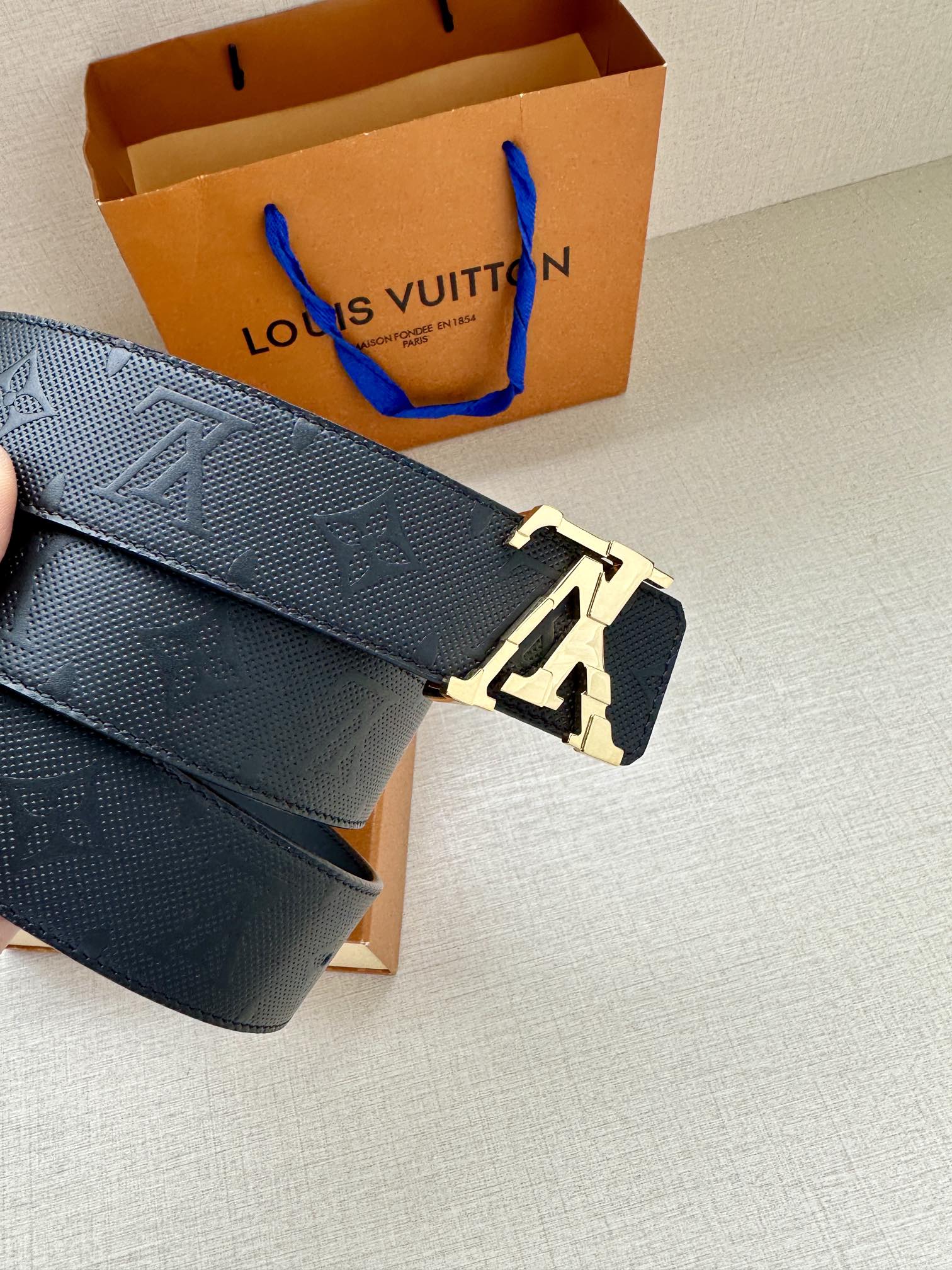 Dark blue leather belt with embossed pattern and silver LV buckle, side view