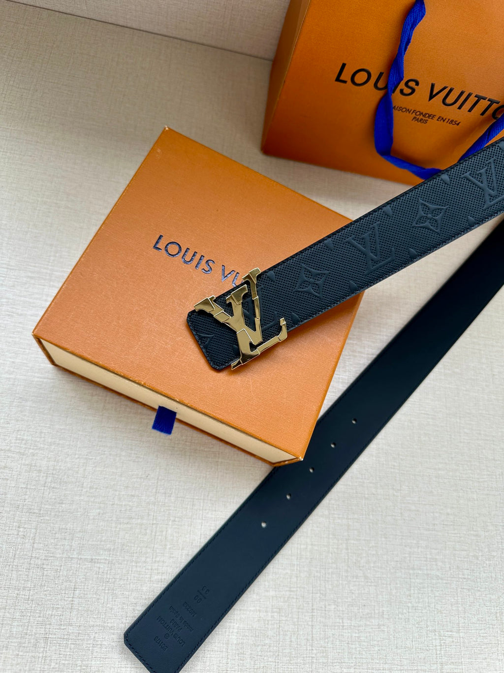 Dark blue leather belt with embossed pattern and silver LV buckle, laid flat