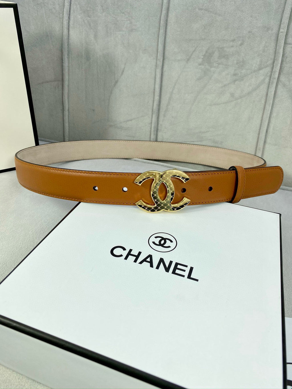 Tan leather belt with gold-tone CC buckle, shown across a white gift box