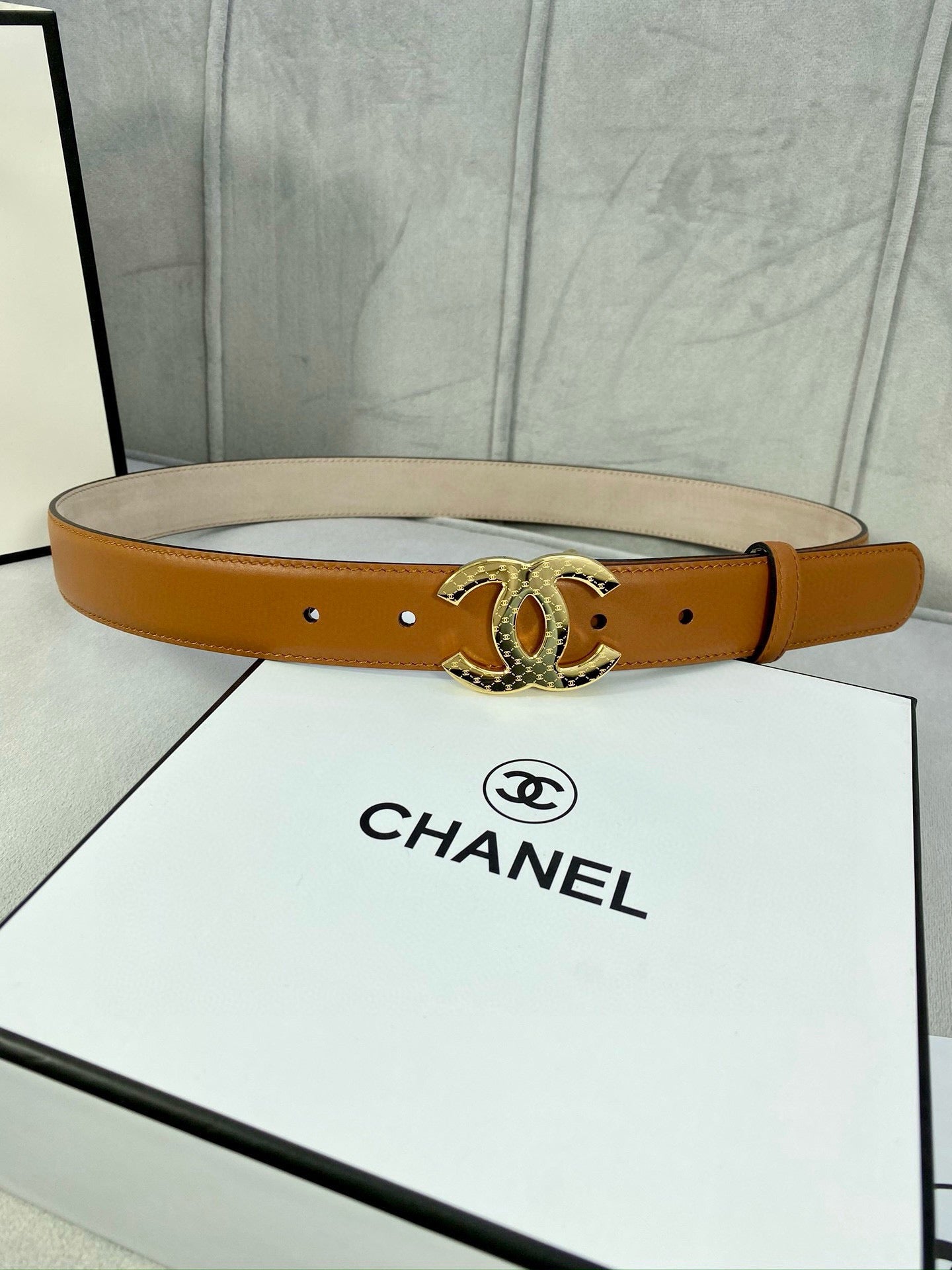 Tan leather belt with gold-tone CC buckle, shown across a white gift box