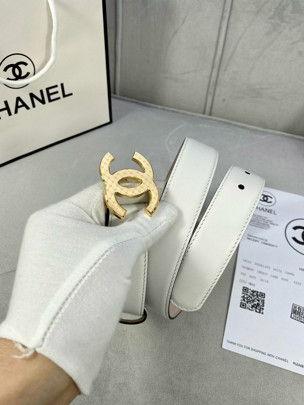 White leather belt with gold-toned CC buckle shown on a display box