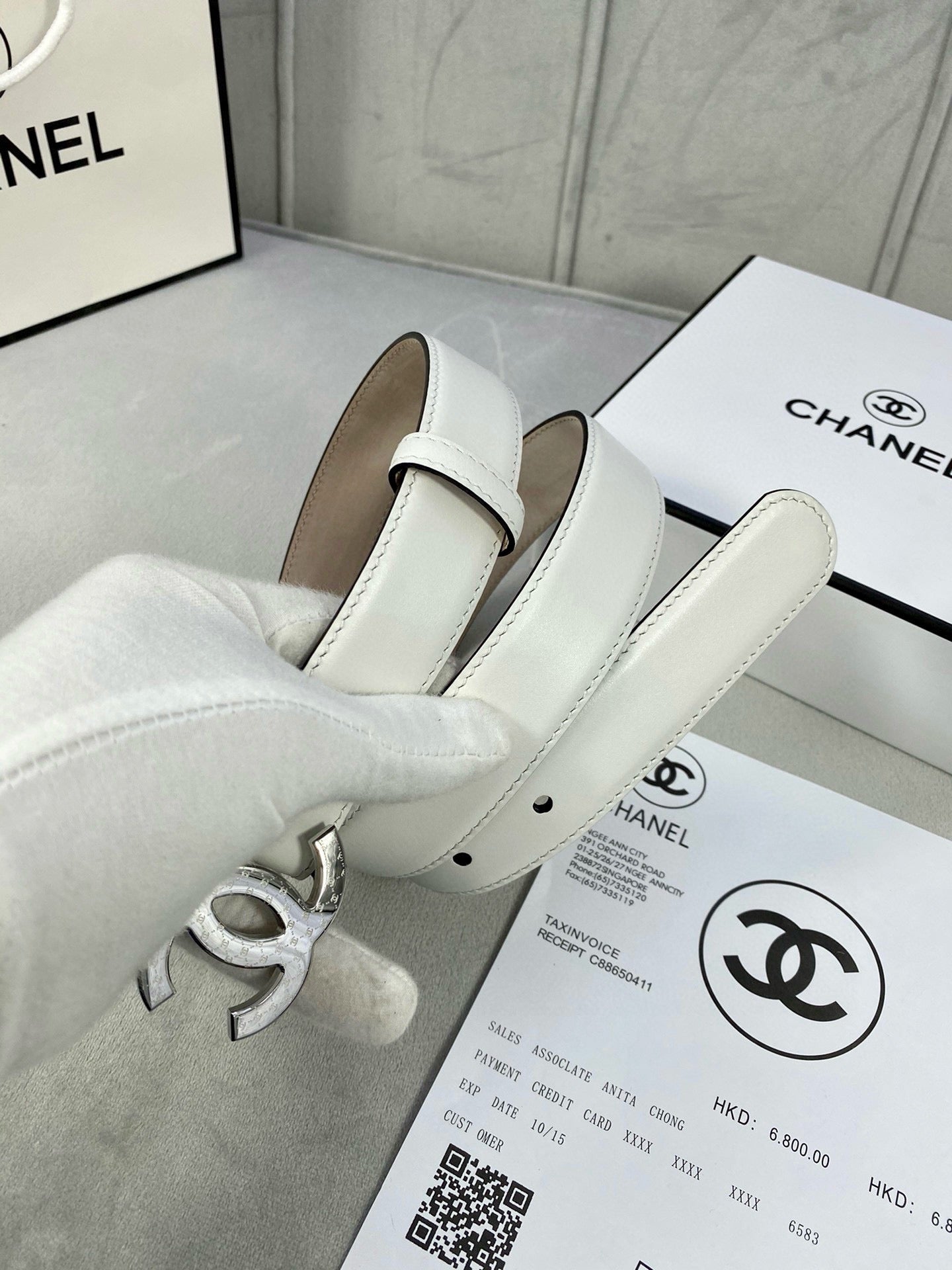 White leather belt with silver-tone CC buckle and folded strap on box