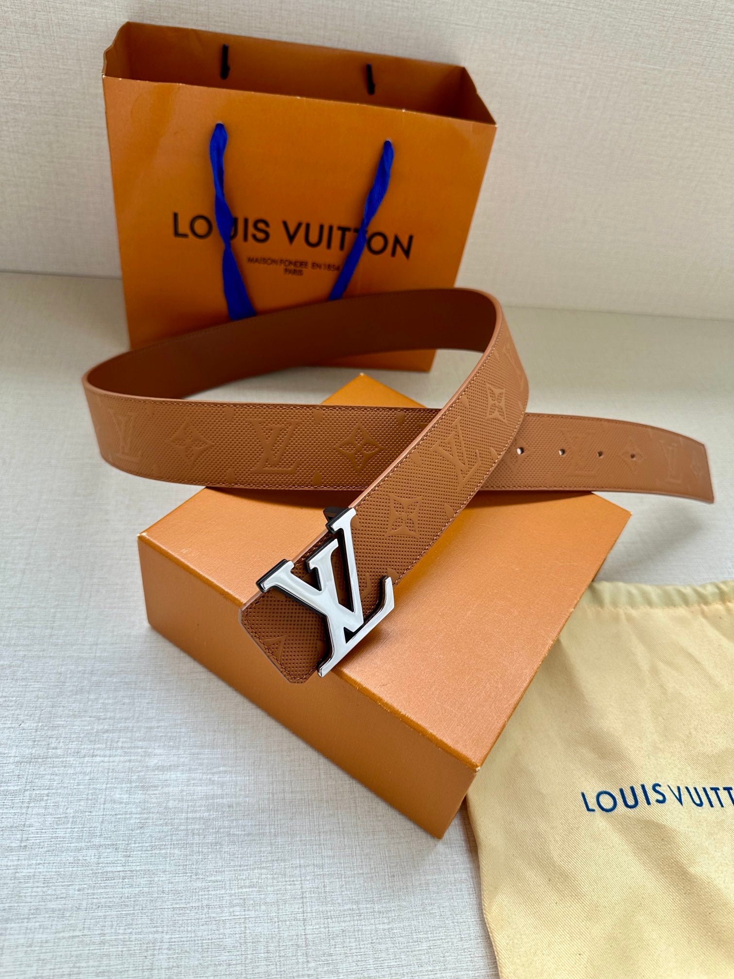 Tan Louis Vuitton belt with monogram strap and silver LV buckle laid flat