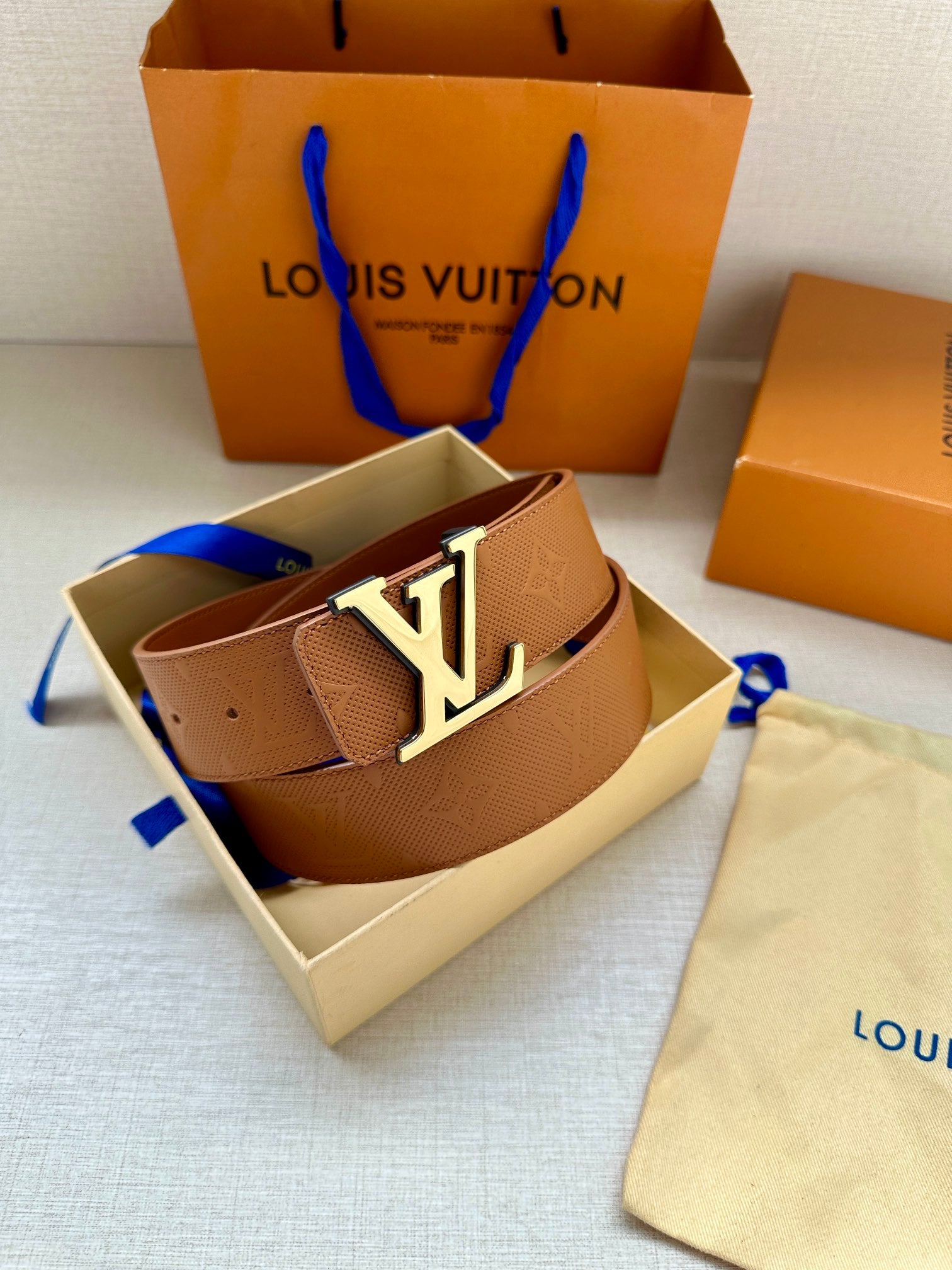 Light tan Louis Vuitton belt with monogram strap and silver LV buckle, angled
