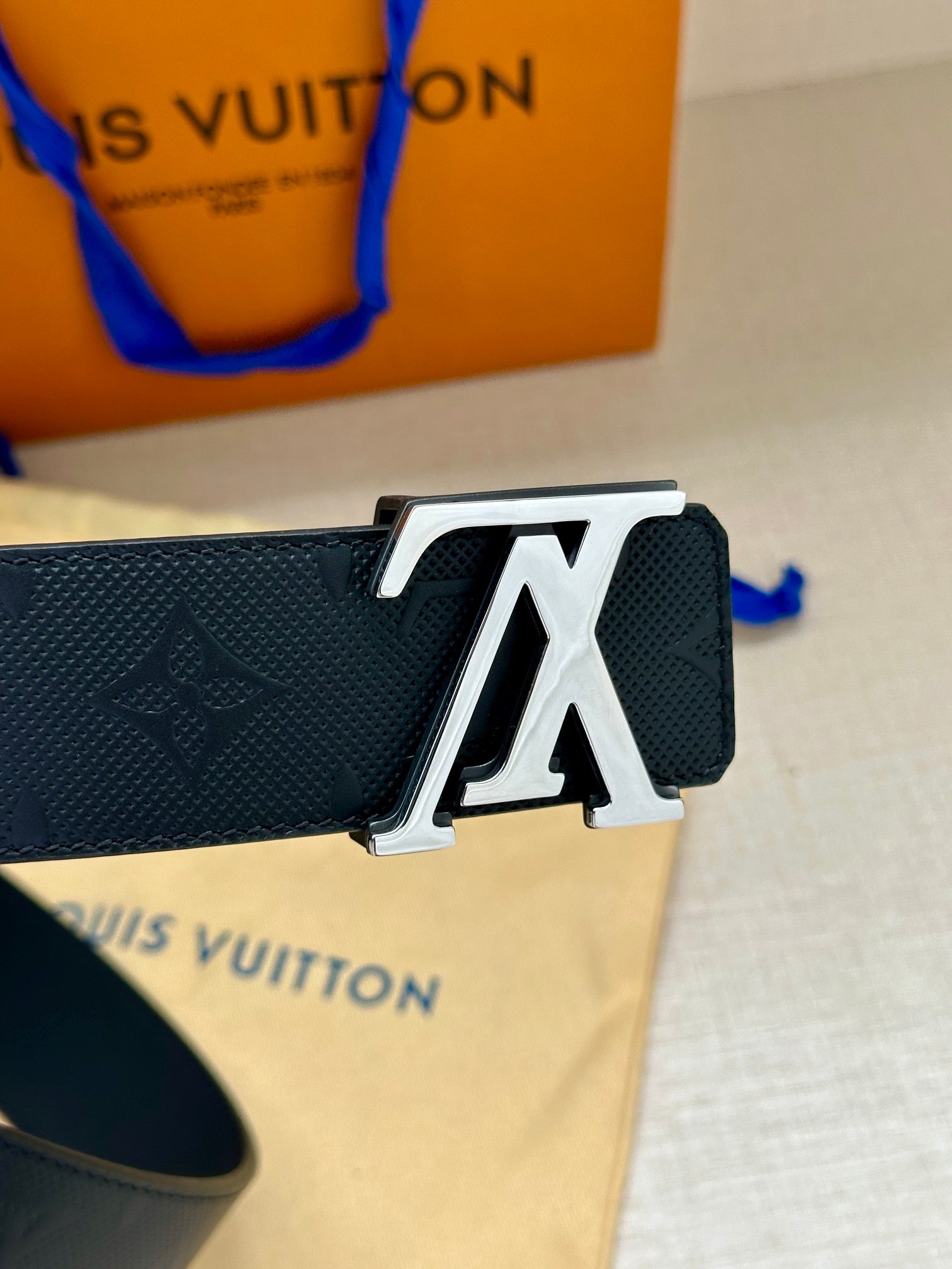 Louis Vuitton belt buckle close-up: dark navy embossed leather with gold LV emblem