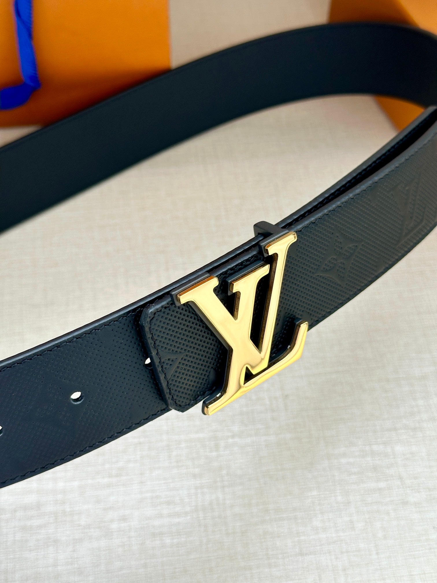 Louis Vuitton belt close-up: dark navy embossed strap with gold LV buckle hardware
