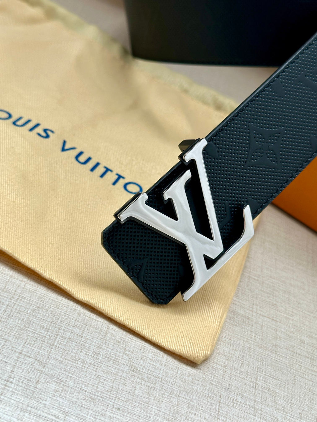 Louis Vuitton belt buckle detail: dark navy embossed strap with gold-tone LV plaque