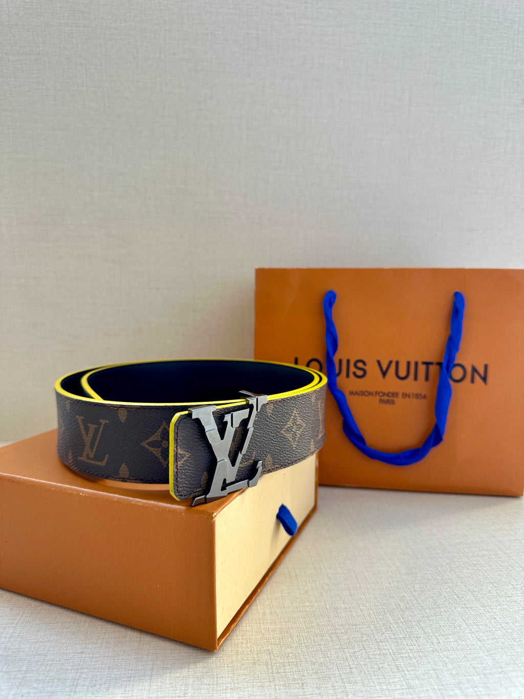 Louis Vuitton monogram belt with gold buckle, blue edge trim, angled view