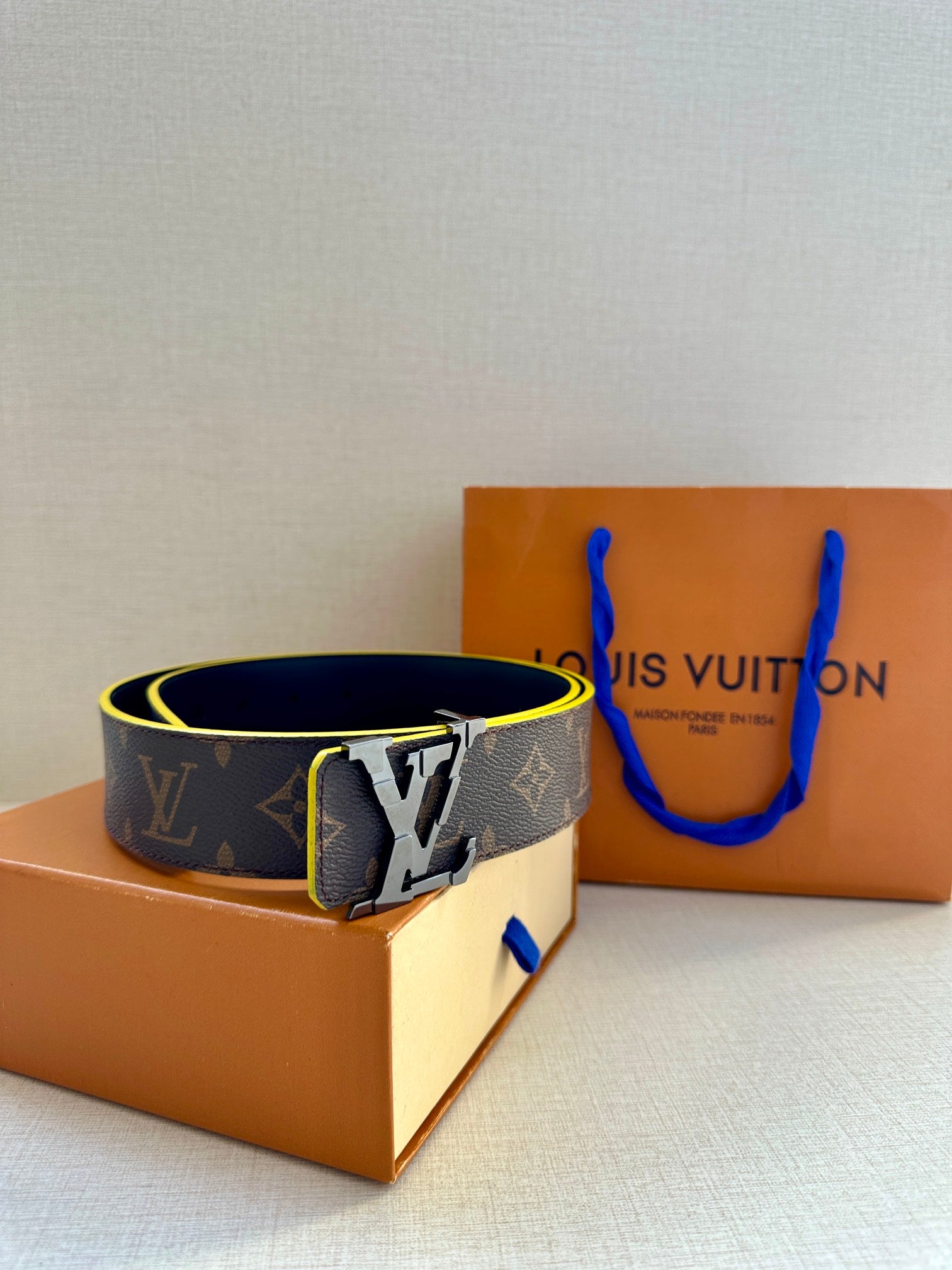 Louis Vuitton monogram belt with gold buckle, blue edge trim, angled view