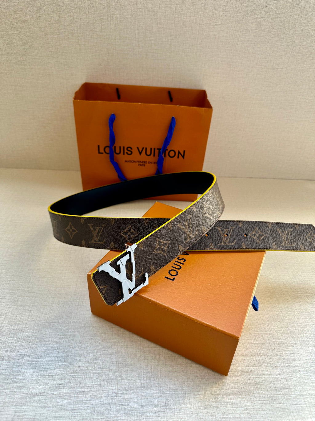 Louis Vuitton monogram belt with gold buckle and blue edge trim, laid across