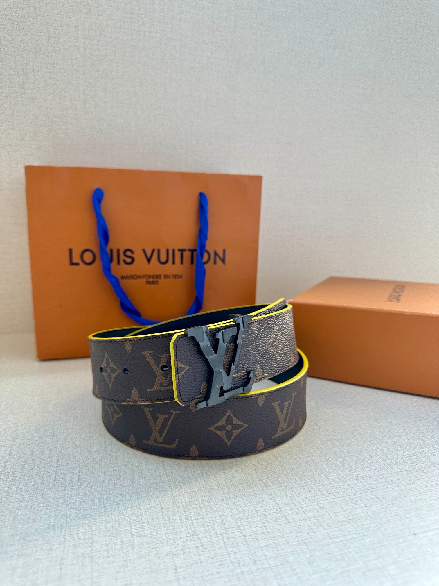 Louis Vuitton belt with monogram pattern, dark strap, gold buckle, and yellow trim