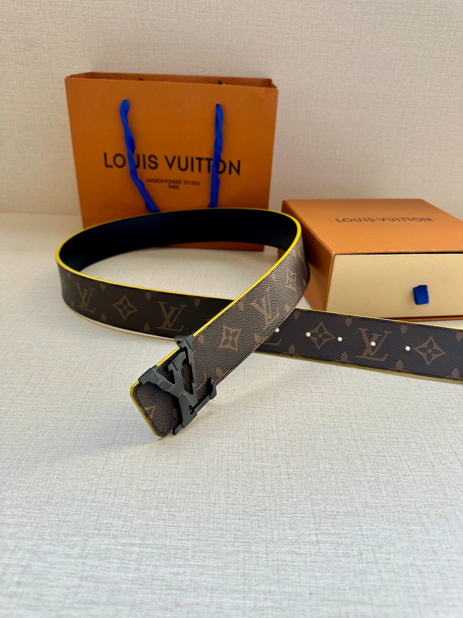 Louis Vuitton belt with dark monogram strap, gold buckle, and bright yellow edge
