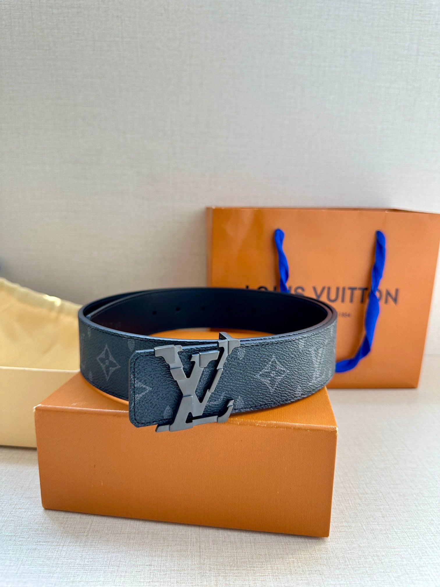 Dark monogram belt with silver-tone buckle and curved strap, side view