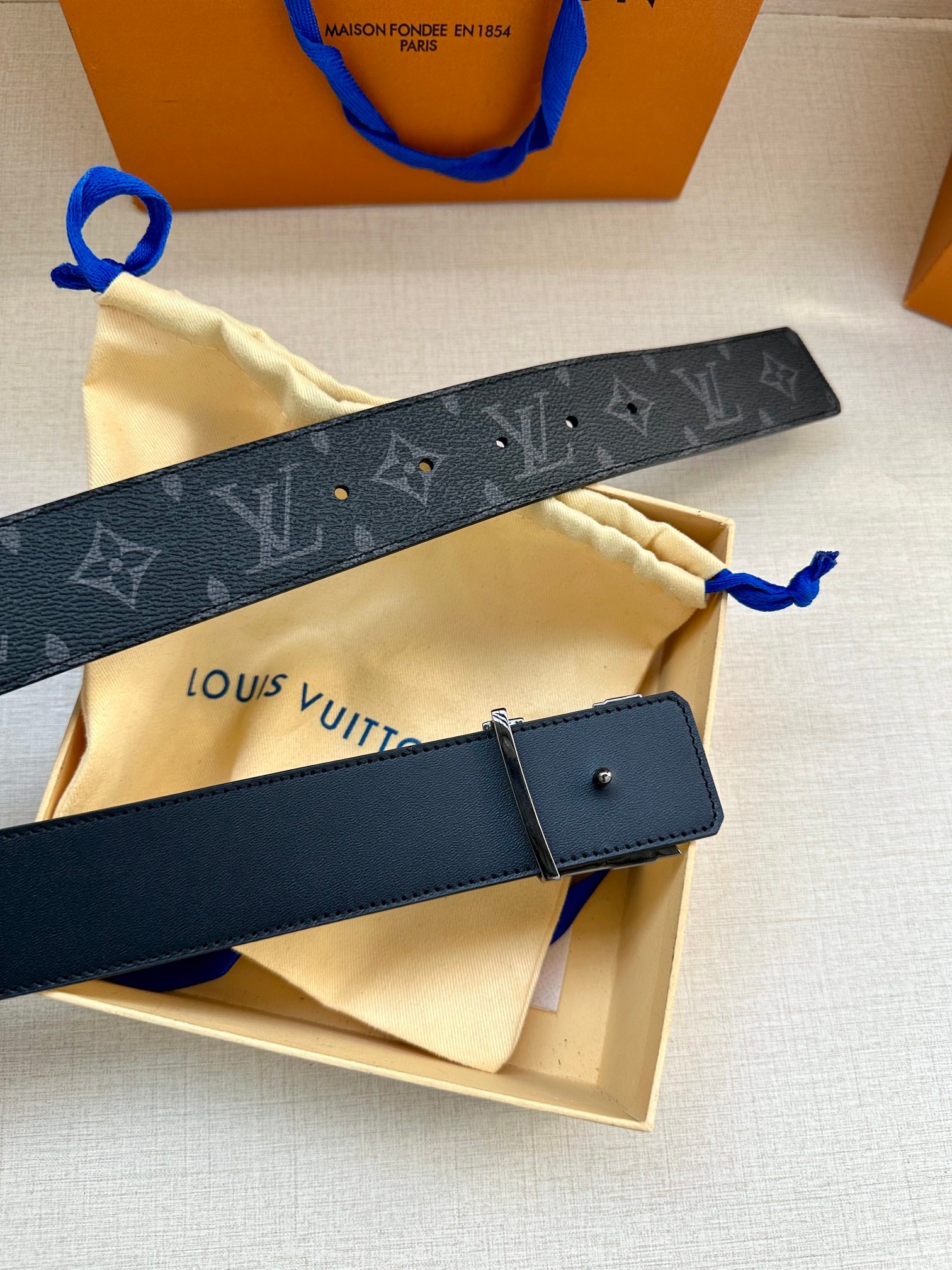 Louis Vuitton monogram belt with dark strap, silver buckle, and blue pull loop.