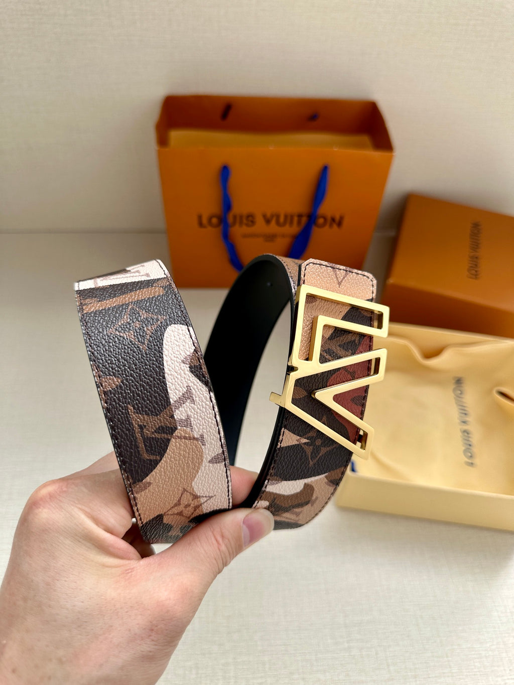 Designer belt detail: patterned strap with gold-tone LV buckle and black underside