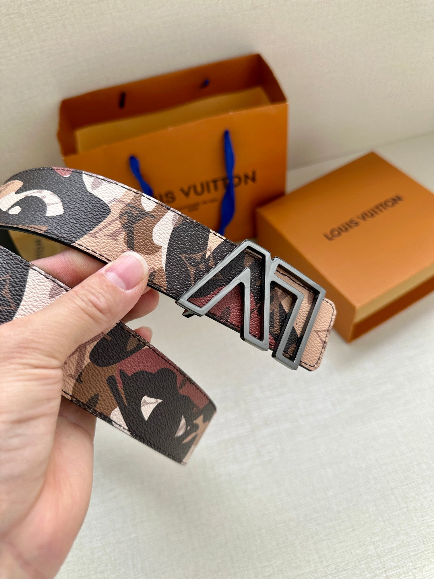 Designer belt close-up with gold-tone LV buckle on printed logo-style strap